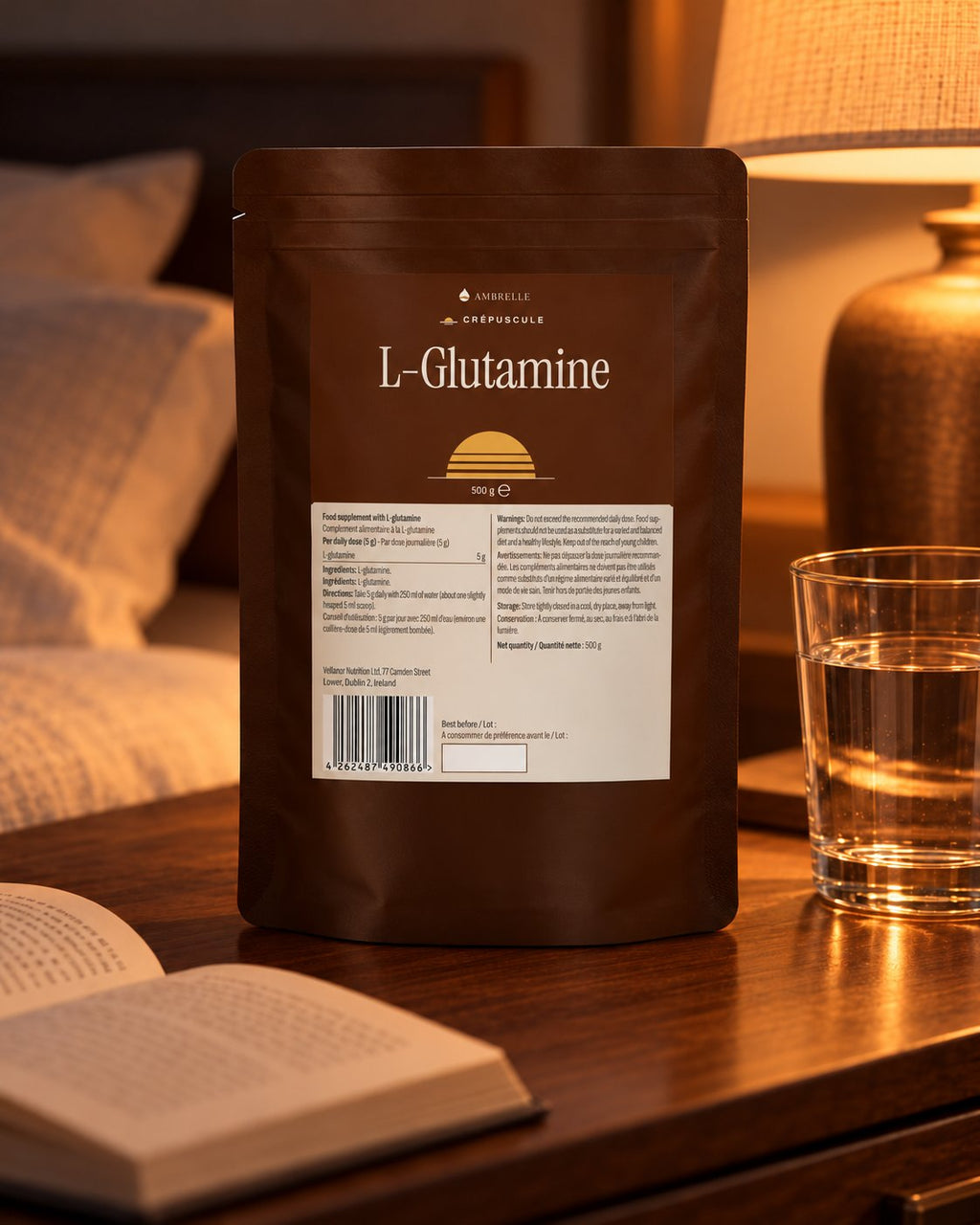 L-Glutamine Powder by AMBRELLE on a walnut bedside table lit by a lamp, with an open book