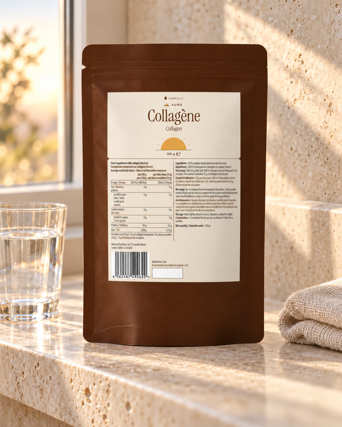 Sachet de collagène en poudre AMBRELLE sur une étagère de salle de bains en travertin, au lever du soleil, avec un verre d'eau