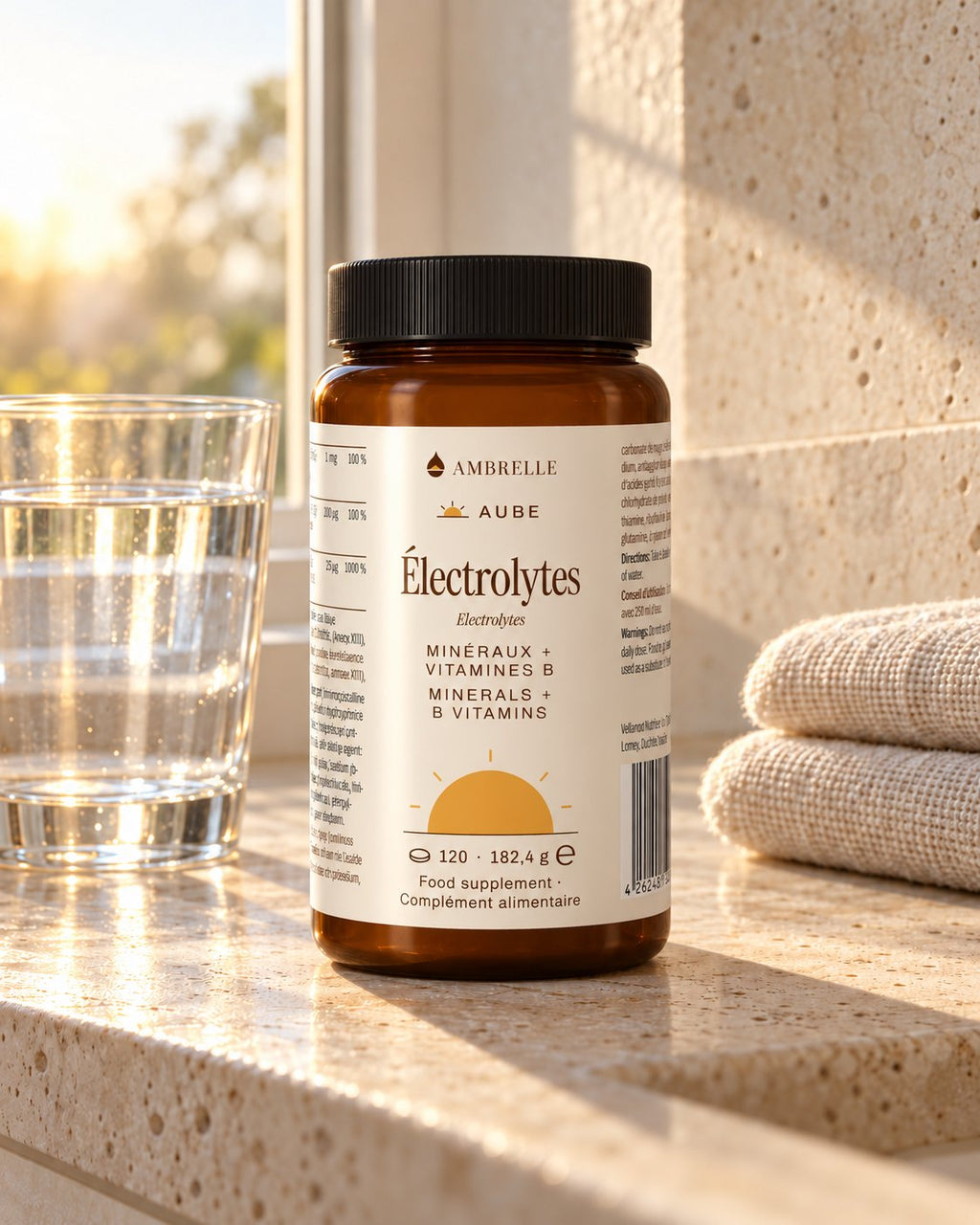 Elektrolytencomplex-tabletten van AMBRELLE op een badkamerplank van travertin bij zonsopgang, met een glas water